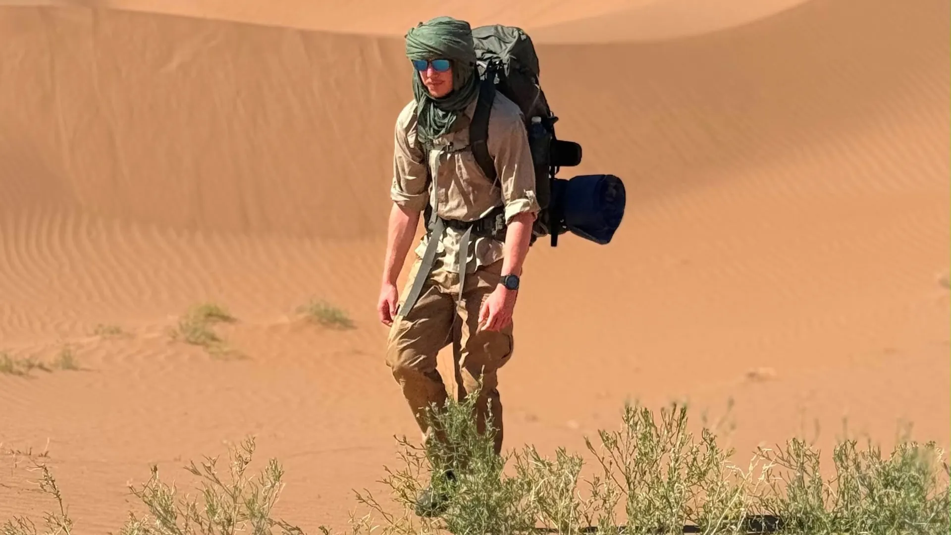 Tim Jambor with backpack, sunglasses and headscarf in the dunes of the Sahara